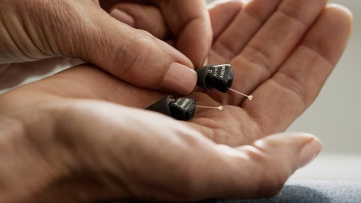 A person holds a pair of small hearing aids