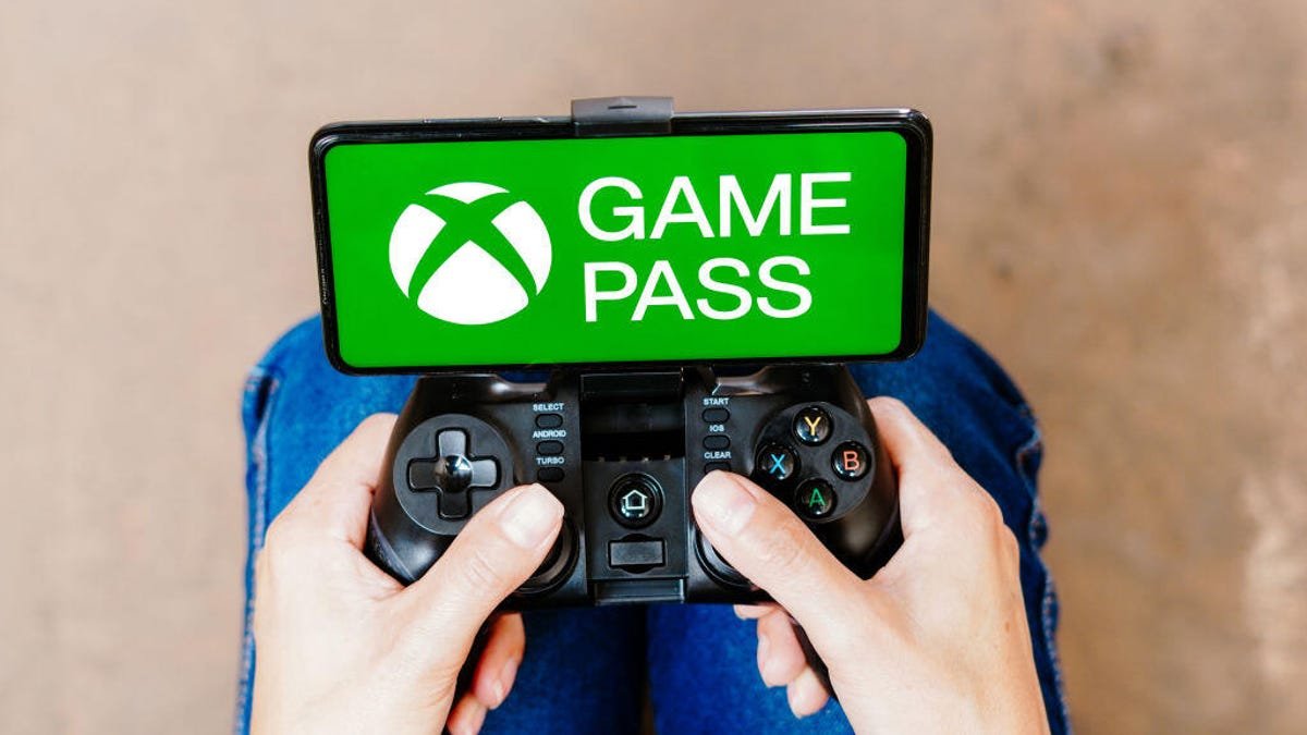 A person holding a game controller connected to a smartphone. The Xbox Game Pass logo is on the smartphone