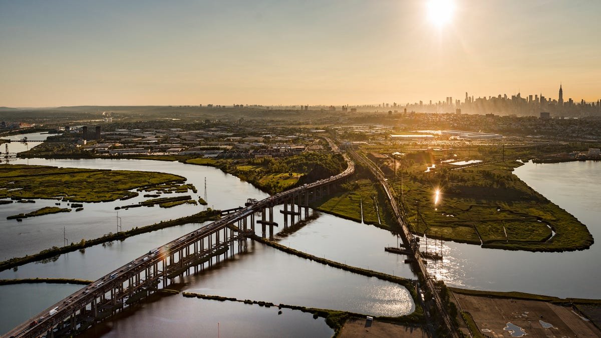 Aerial view of Newark, NJ with a bright sun in the sky and the Manhattan skyline in the distance.