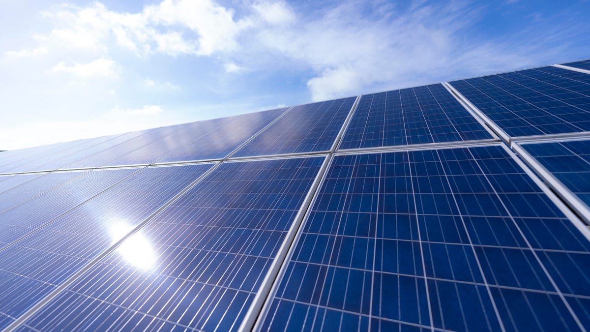 A dramatic, low-angle view looking up at solar panels, with a blue sky and white clouds beyond.