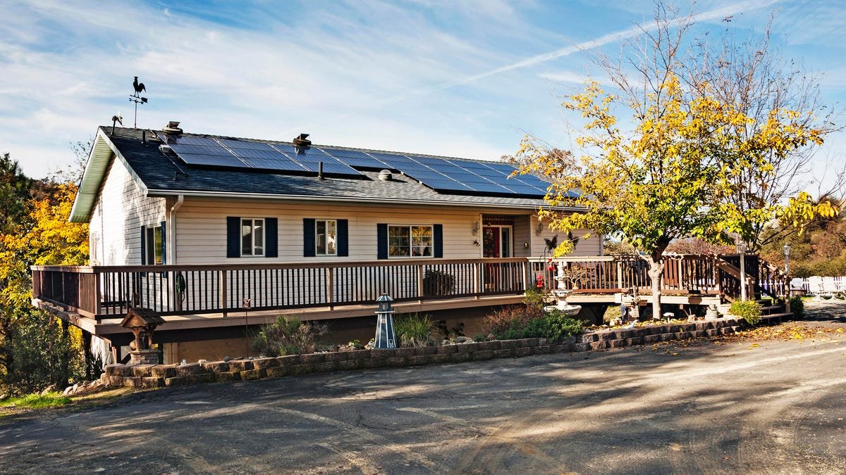 A white house with a deck on two sides and solar panels on the roof.