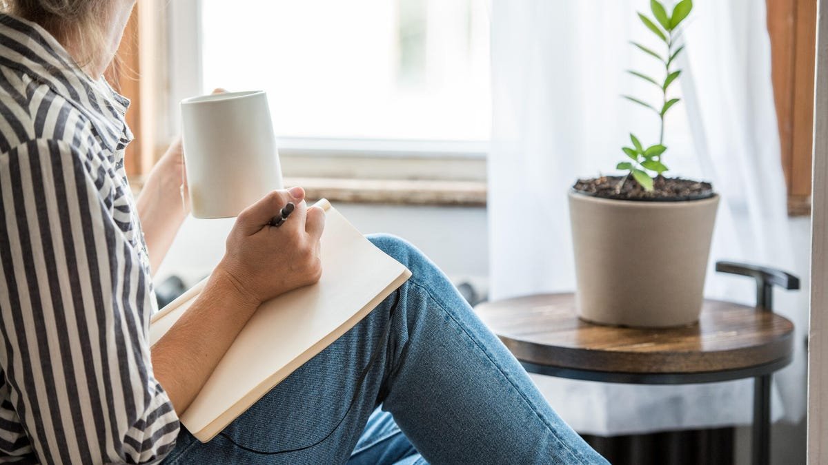 Woman journaling and drinking herbal tea next to a house plant